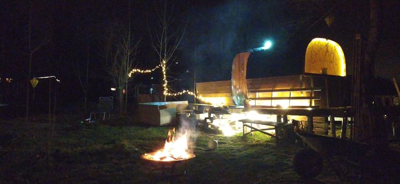 Fasssauna bei Nacht mit Lagerfeuer und Lichterketten